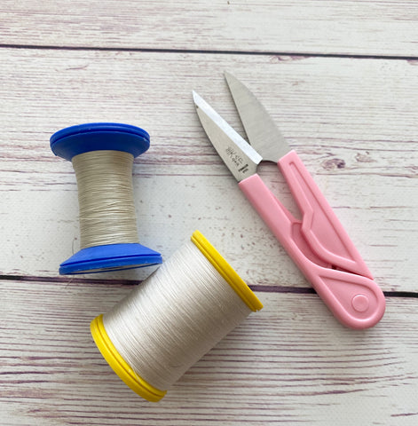 two spools of neutral shade thread lie on a timber surface with a pair of thread snips with pink handles