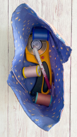 an overhead shot of the interior of the posh knot bag.  Inside the bag is  large rotary cutter , pretty spools of thread and a fabric marking pencil