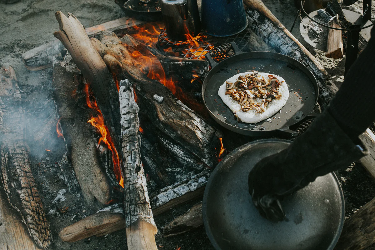 Person cooking pizza on open fire with Barebones gloves and Barebones cooker