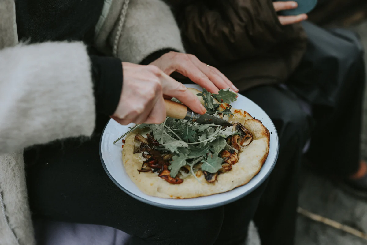 woman cutting pizza outside on falcon enamelware plate with opinel knife