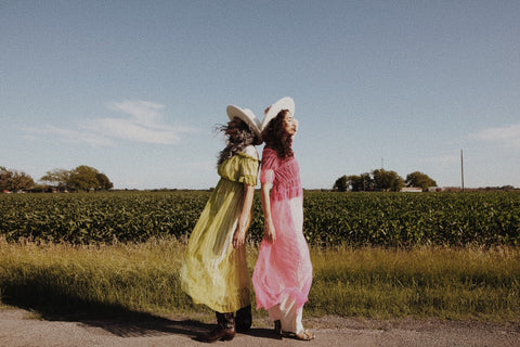 two girls standing by a field with pink and green dresses on