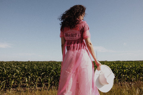 girl standing in field with pink dress on holding a hat