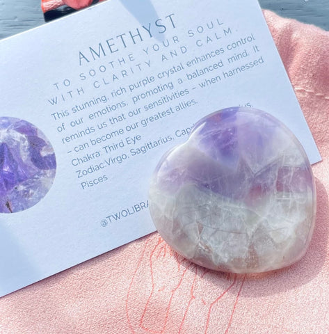 Heart shaped pale purple amethyst stone with a meanings card on top of a pale pink suede pouch