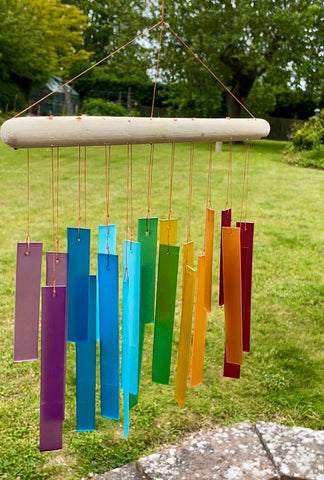 Rainbow coloured rectangular glass decorations hanging on windchime in garden