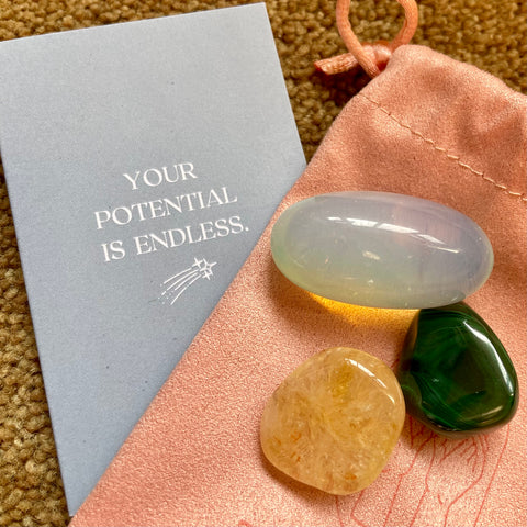 Three crystals - yellow, green and translucent, on a pale peach suede pouch, next to a grey motivational card