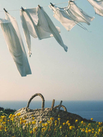 Bohemia Design Beldi Basket hung up on a washing line on a blue sky day with white linen clothes blowing in the wind
