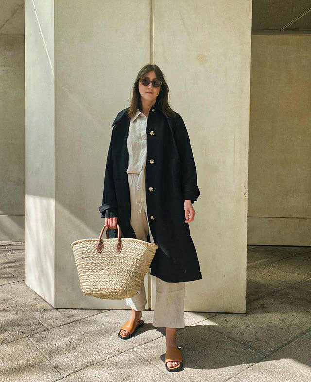 Woman in a navy trench coat and sunglasses holding a Bohemia Design basket
