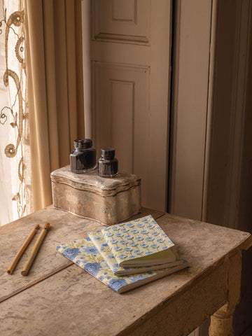 Sage green and blue block printed notebooks on a wooden desk with ink pots