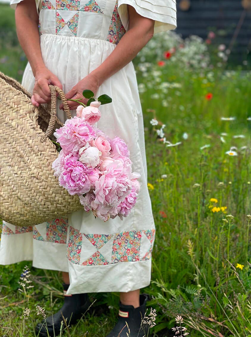 Woman in a white dress holding a Bohemia Design basket filled with pink flowers