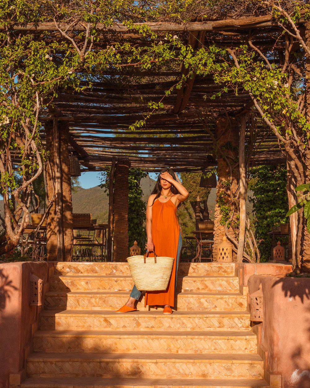 Woman in an orange top holding a Bohemia Design basket bag on terrace steps