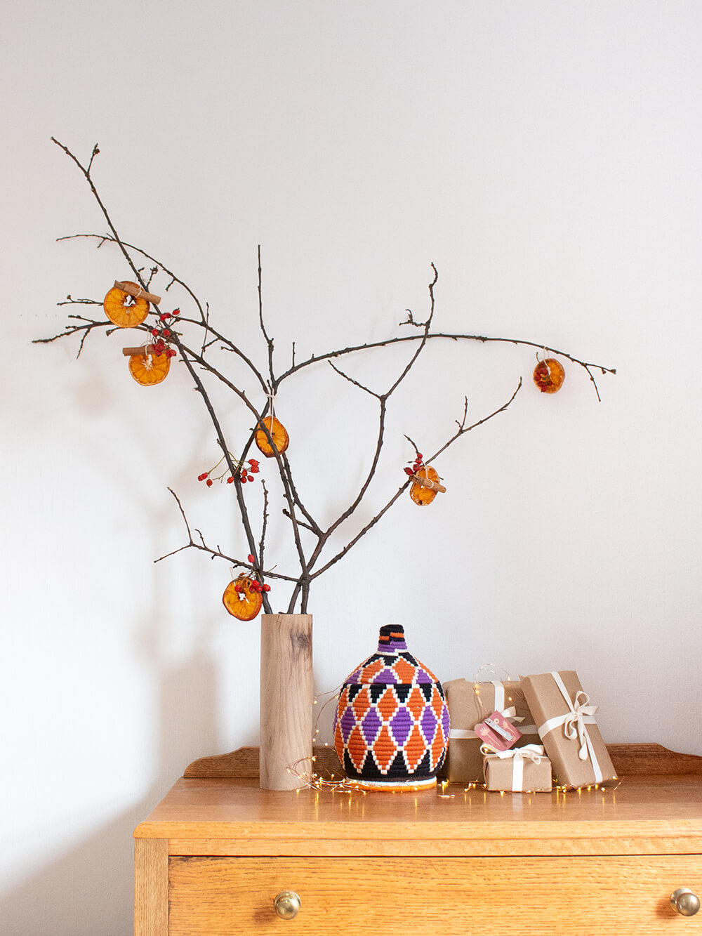 A branch christmas tree with dried orange ornaments beside a pile of wrapped gifts from Bohemia Design