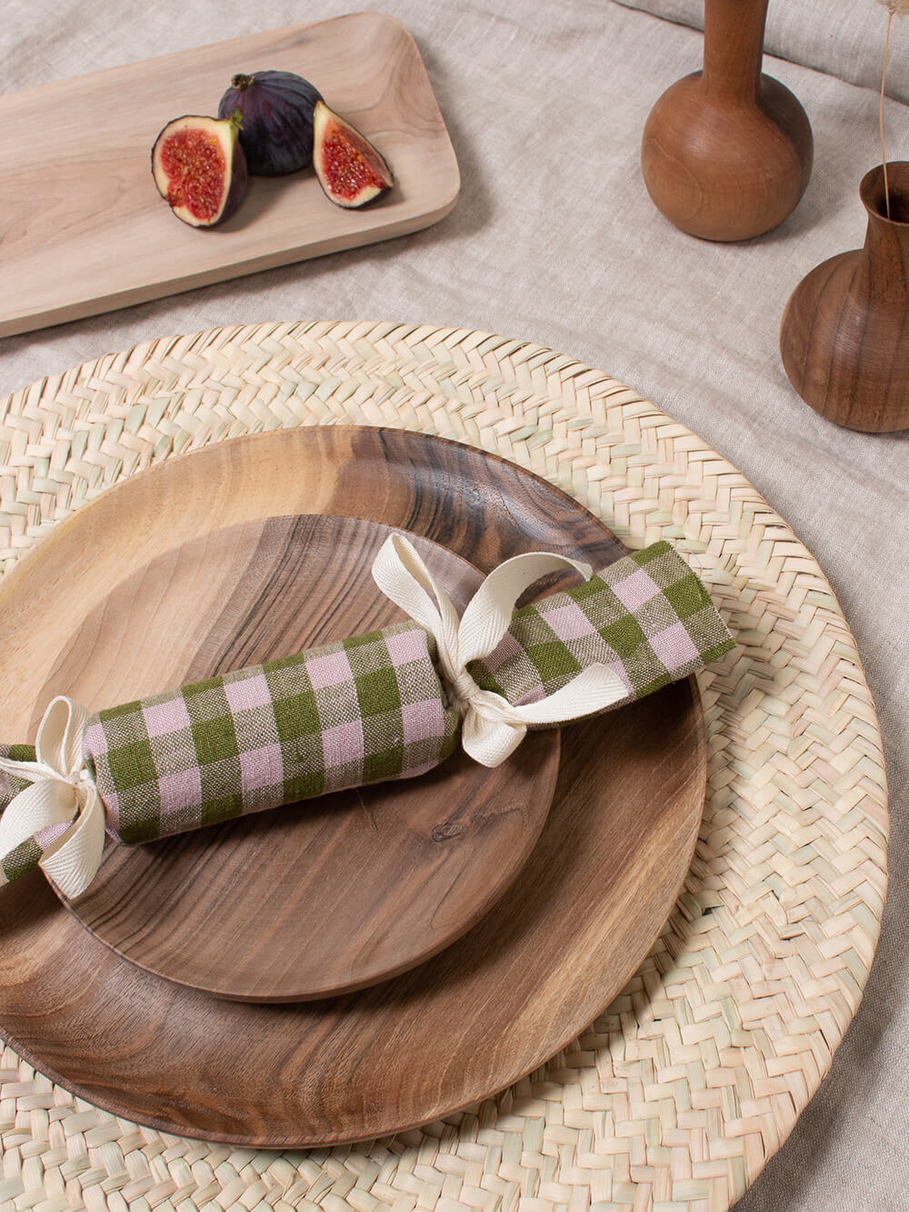 Wooden plates with a christmas cracker made of soft gingham fabric, on woven placemats and natural linen tablecloth