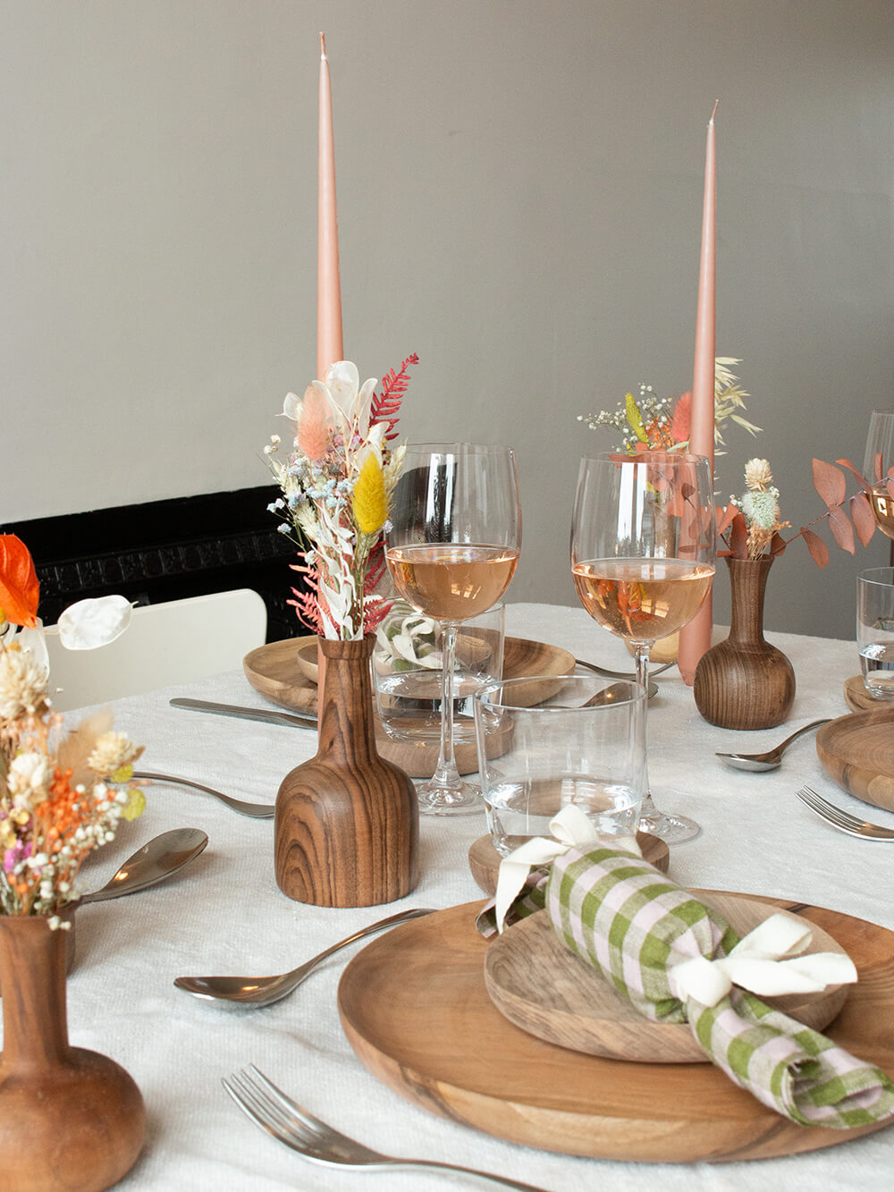 A table set for christmas dinner with wooden tableware, pink candles and rose wine