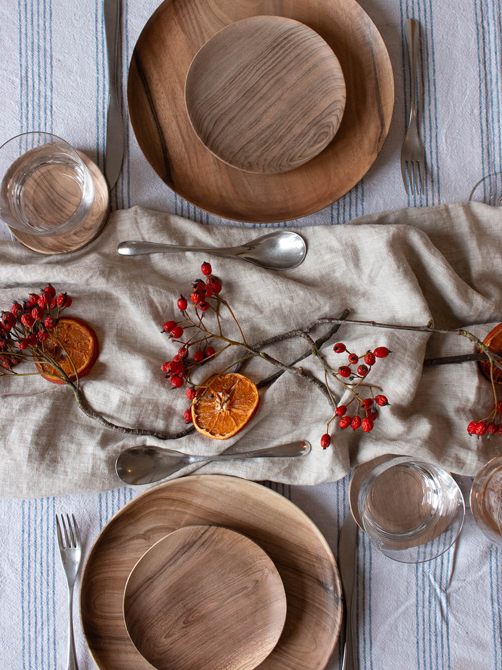 A table set for christmas with neutral linen tablecloth, wooden tableware, and red berry decorations