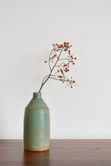 Green textured ceramic vase with sprig of red berries