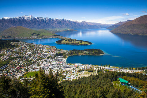 Aerial view of Queenstown, New Zealand. white buildings alongside a large body of water and mountains in the distance.