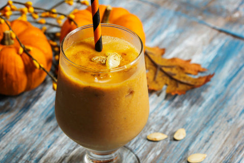 pumpkin smoothie with roasted pumpkin seeds on top and a black and orange straw
