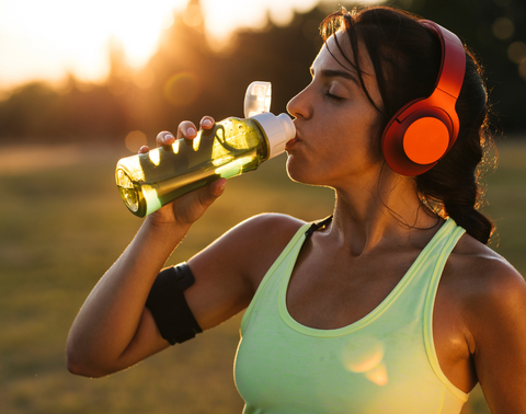 Girl taking a drink of electrolytes from a bottle whilst running