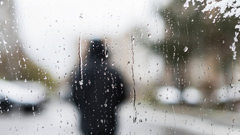 drops of water on window with person in background blurred out in black coat