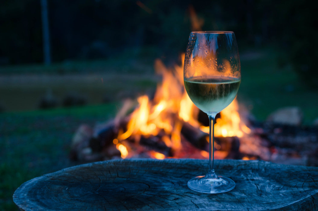 Glass of wine on a log in front of camp fire