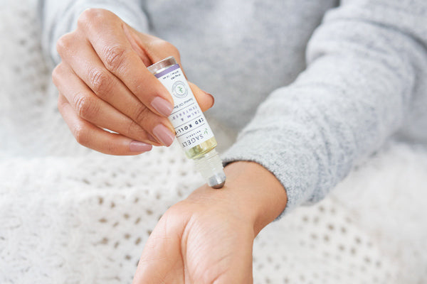 A woman wearing a grey sweater using the Sagely Naturals Calm & Centered CBD Roll On on her wrist.
