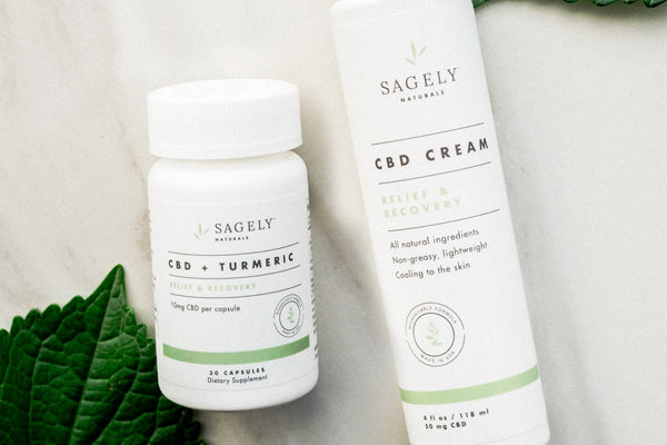 Sagely Naturals Relief & Recovery CBD Capsules and CBD Cream on a table with a mint leaf.