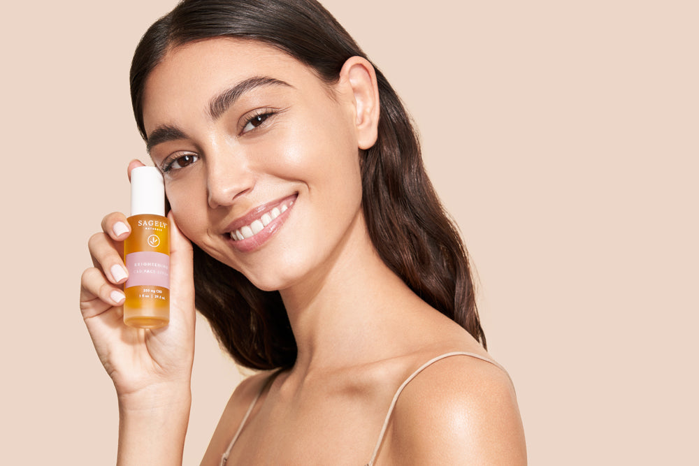 A woman holding Sagely Naturals Brightening CBD Serum and smiling