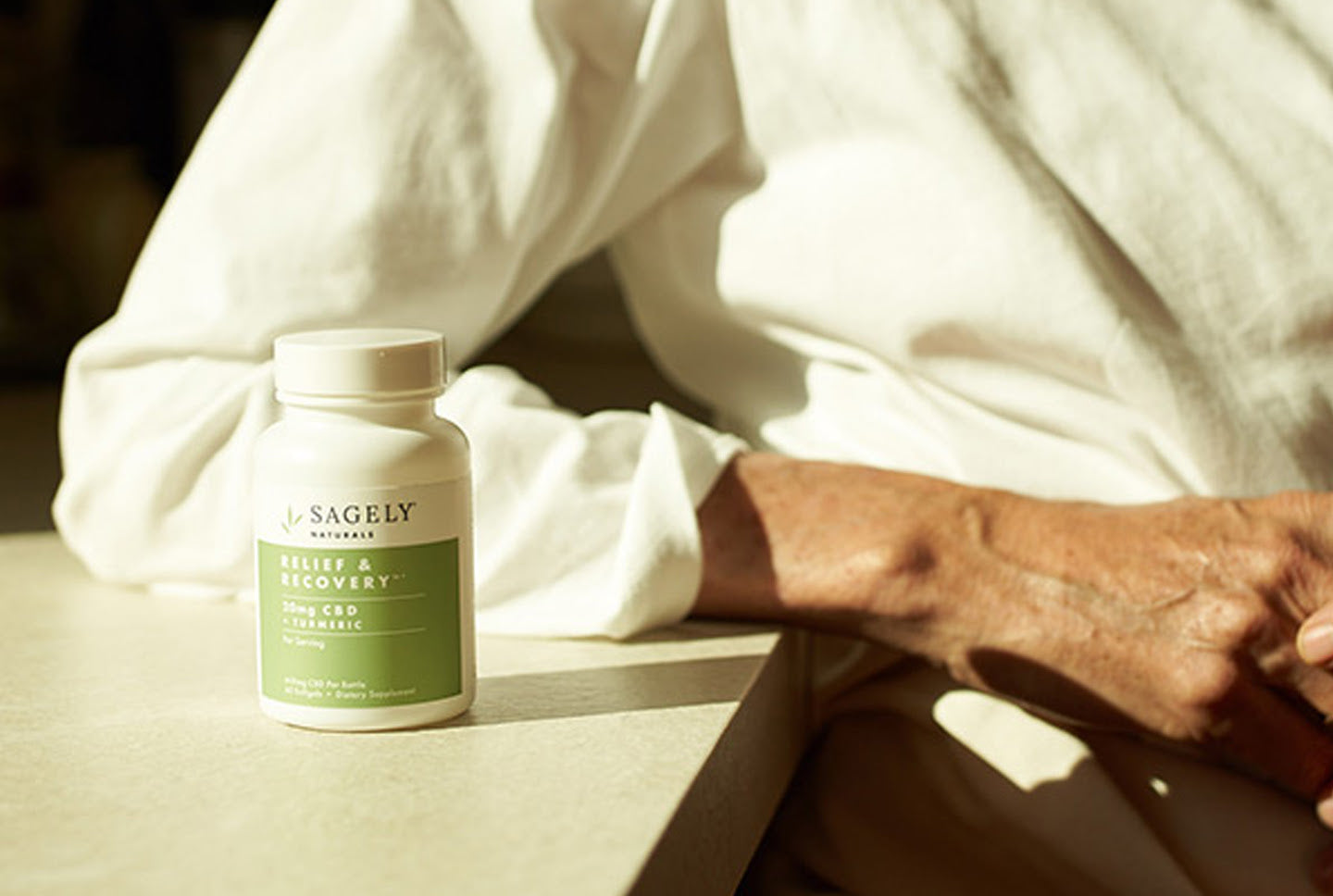 A woman sitting at her coffee table in front of a bottle of Sagely Naturals Softgels.