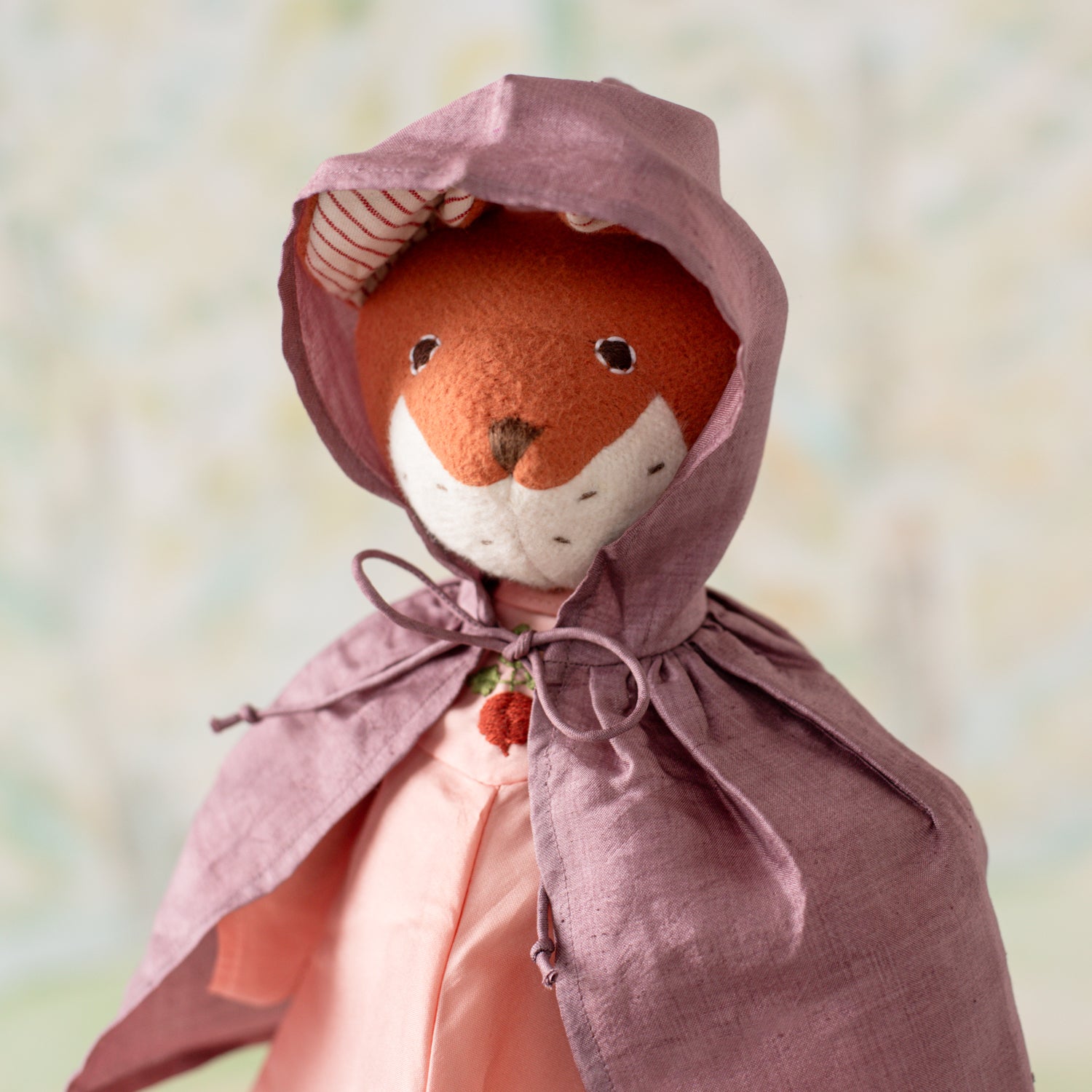 Portrait of Flora Fox wearing a purple silk cloak, tied at the neck with the hood pulled up, over pink regal radish gown