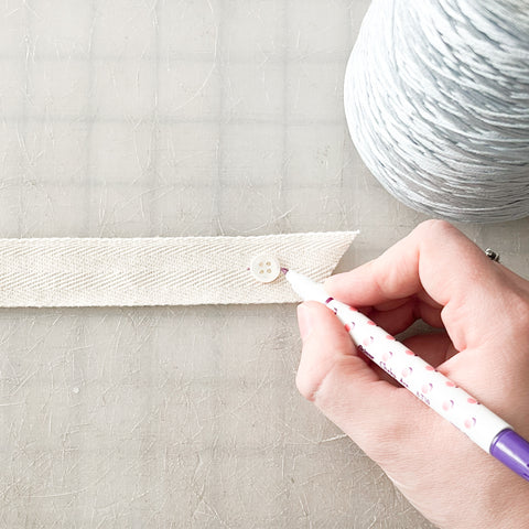 a hand with a pen marking dots on either side of the button on the sash