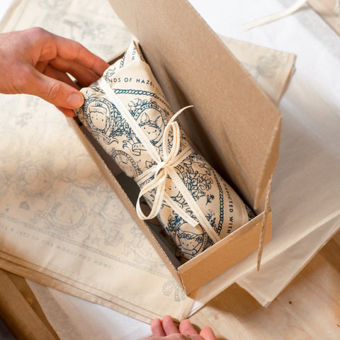 A Hazel Village doll wrapped in a bandana, preparing to be packaged into a recyclable box for shipping.