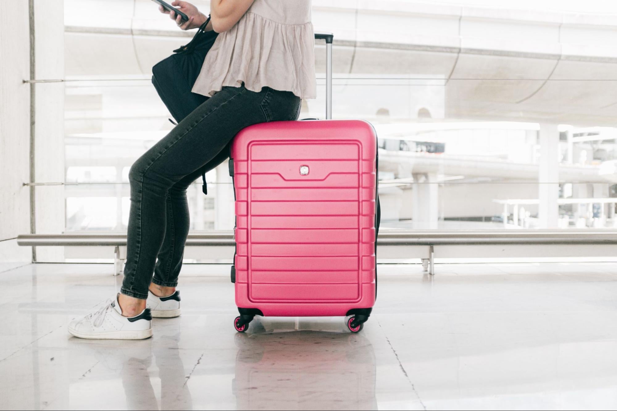 Cropped image of a woman sitting on a pink suitcase 