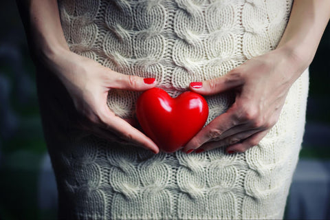 A cropped photo of a woman holding a small heart in front of the vaginal area