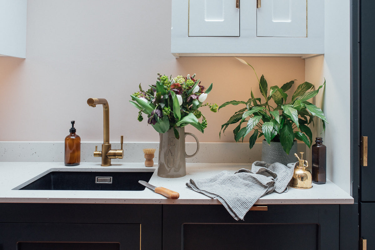 a kitchen sink with marble counters, plants and striped linen