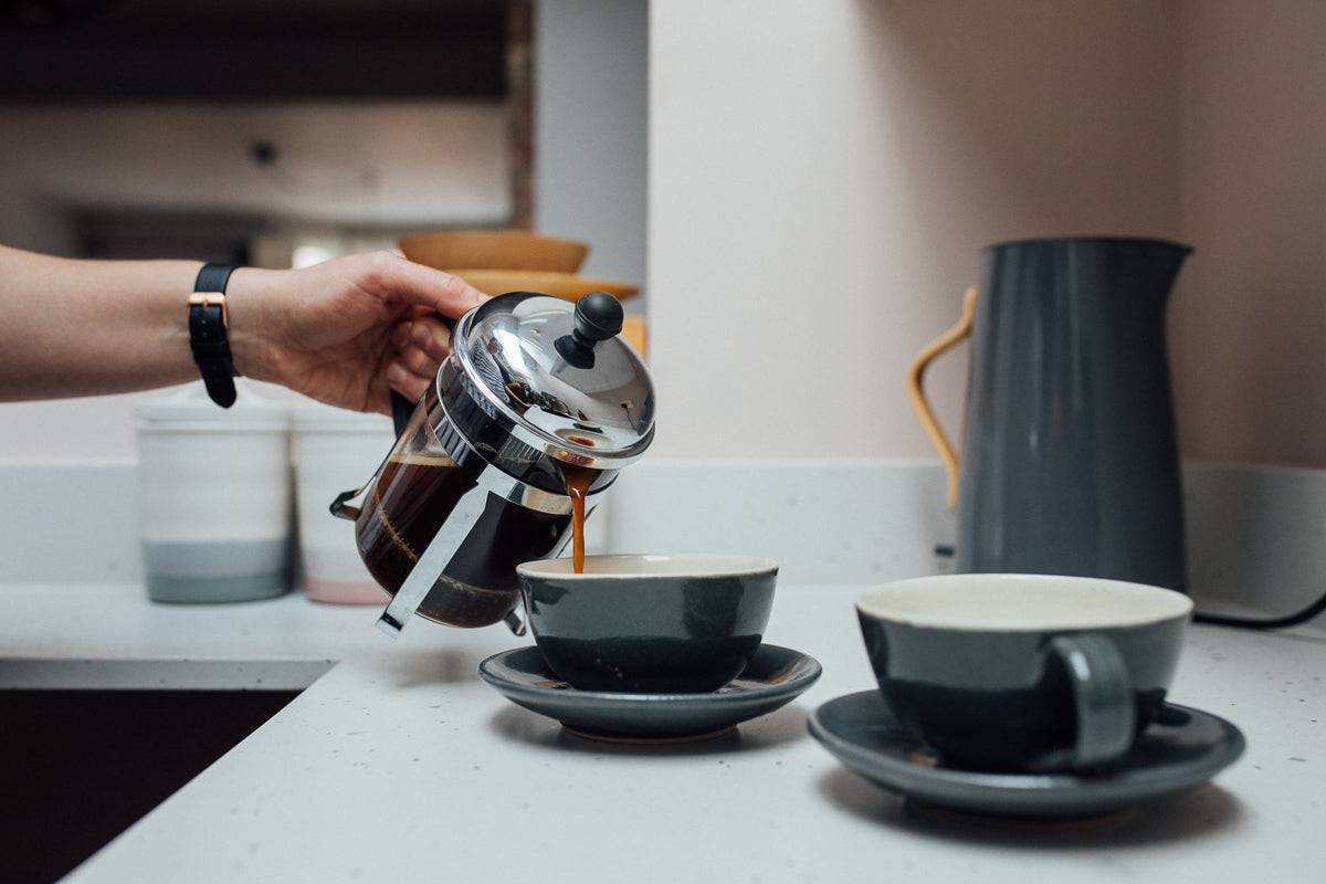 Two grey coffee cups and a hand holding a cafetiers