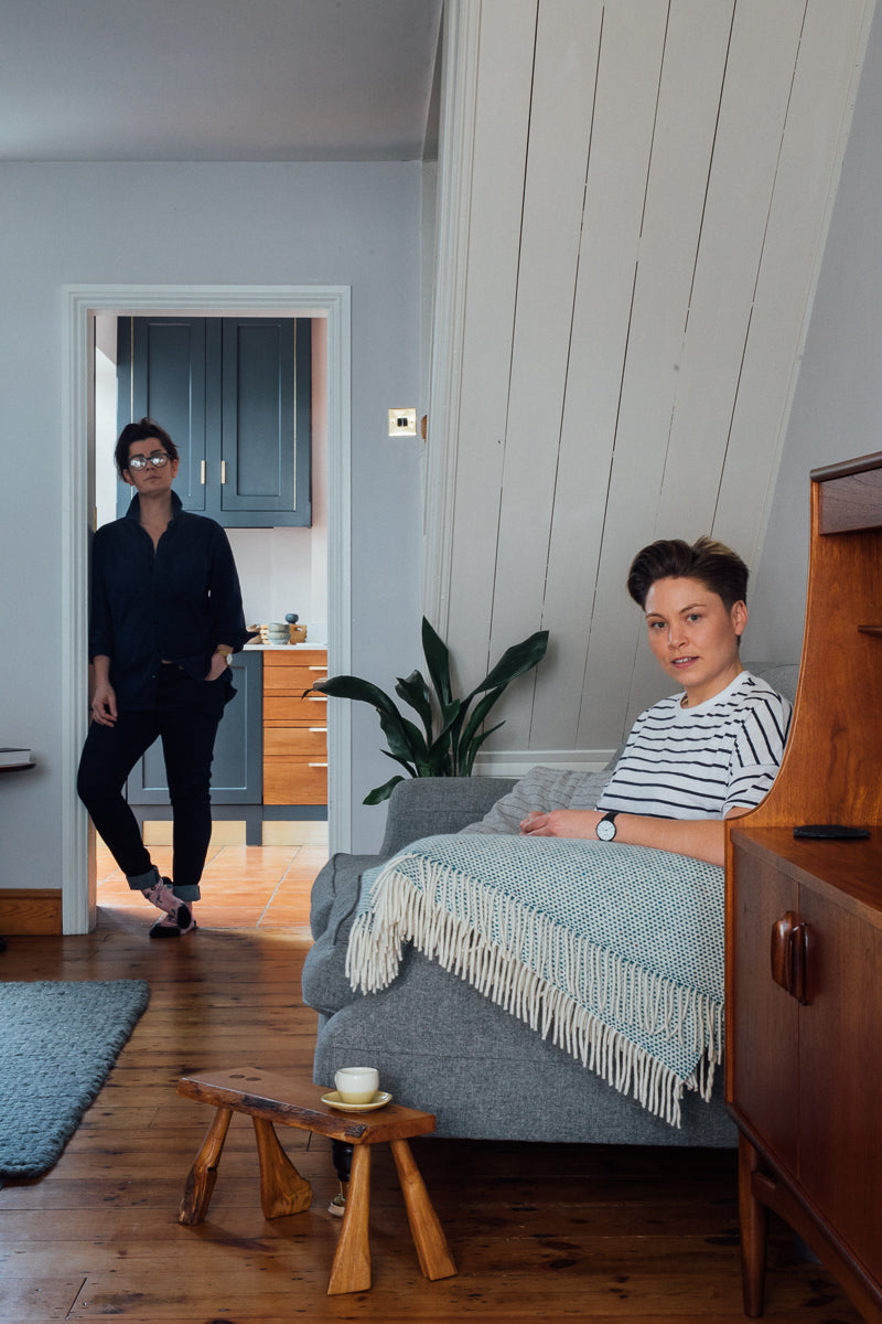 a woman sits on a grey sofa in front of an organic shaped wooden stool