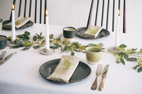 A table laid with grey plates and cream napkins with green foliage