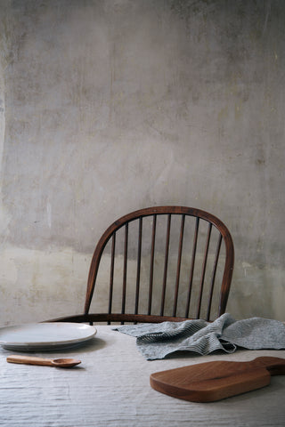 a rounded back spindle chair behind a table covered with linen