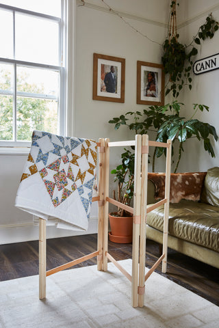 A wooden drying rack with a quilt hung over it