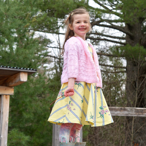 girl outdoor in nature all dressed, dress and handmade sweater up holding a stick