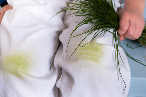 person wearing white pants with grass stains while holding grass in hand 