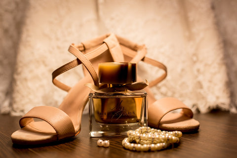Nude heels behind a bottle of perfume and pearl jewellery