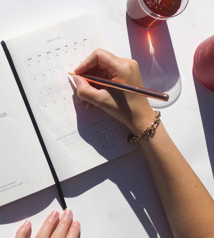 Woman writing out a calendar in a white diary with a glass of Jeuneora Beauty Brain.