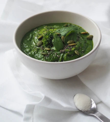 Bowl of green Immune Booster Vegetable Soup with a scoop of unflavoured Naked Marine Collagen peptides powder.