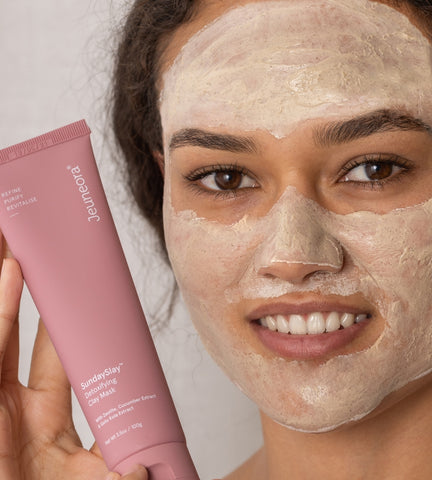 Woman holding SundaySlay tube with detoxifying kaolin clay mask on skin in evening routine.