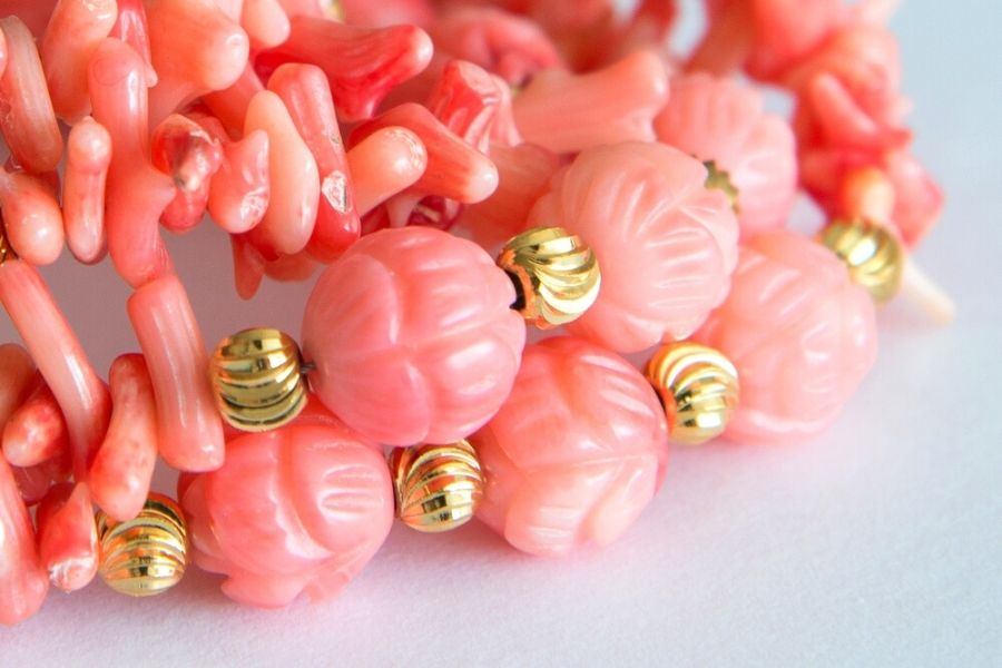 Close up of pink coral jewelry with gold beads.