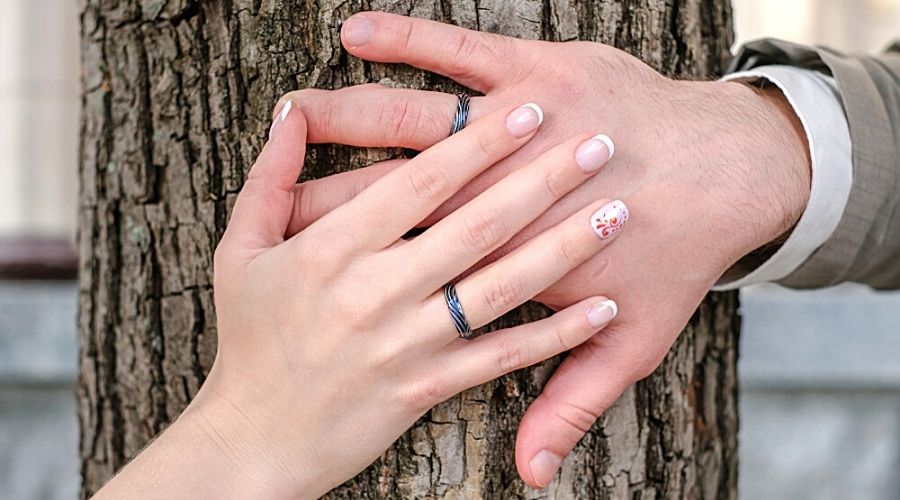 Two hands on a tree showing black gold wedding bands