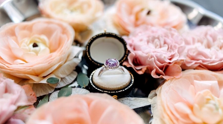 A pink diamond engagement ring in a round box surrounded by pink flowers