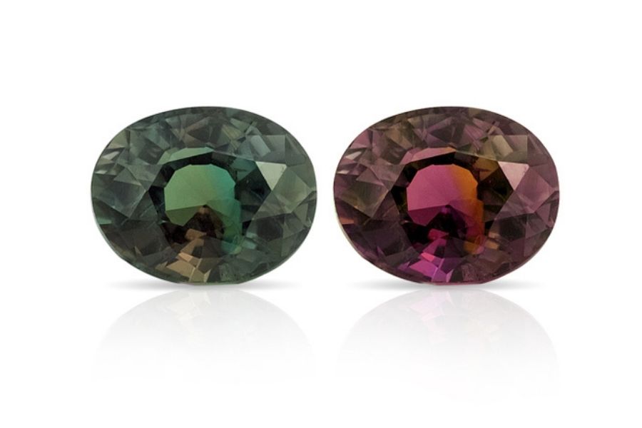 Two alexandrite stones side by side on a white background. One shows the daytime coloration, the other shows the redder nighttime coloration.