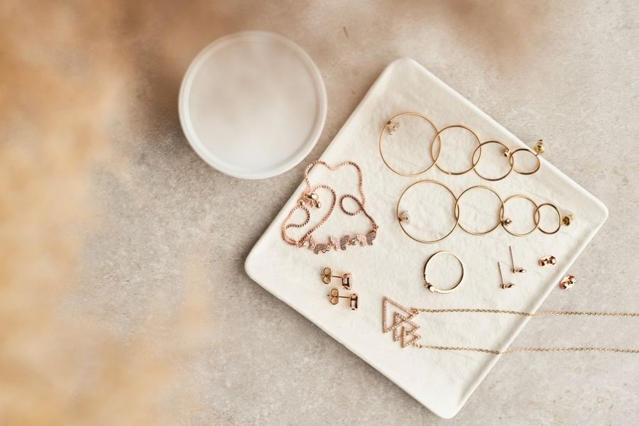 A set of gold jewelry (including rings, necklaces, and several pairs of earrings) on a white marble plate.